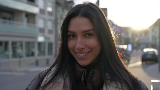 Portrait of a Middle Eastern young woman in her 20s standing in city street looking at camera. Closeup face of a brunette adult girl