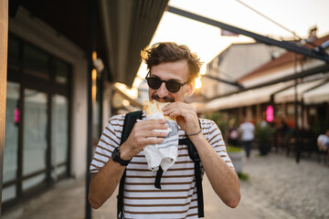 One man young adult modern caucasian male in the city in sunny day walk and eat sandwich fast food...