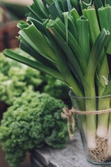 Obraz premium Vertical shot of green garlic in a glass with cabbages in background
