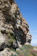 Vertical shot of a steep cliff covered with green moss on a blue sky background