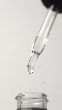 Vertical shot of the oil drops falling from the pipette on the white background