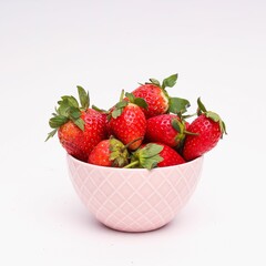 Closeup shot of a pink bowl filled with strawberries in front of a white background