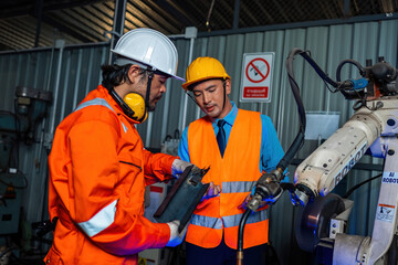 Engineer team service robot welding working in automation factory. People worker in safety suit work robotic arm software programming or replacing part in automated manufacturing industry technology