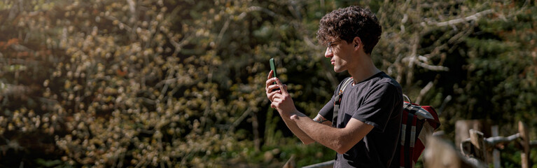 Man traveler standing on bridge and taking photos with smartphone. Rural place. Wild nature.