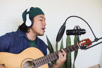 Potrait of Young Asian Man Playing Guitar and Singing during Recording Music At Home