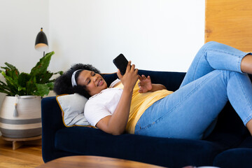 Happy plus size african american woman lying on sofa and using smartphone