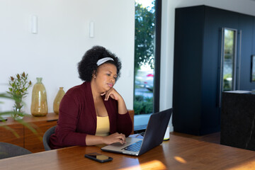 Plus size african american woman sitting at table, using laptop