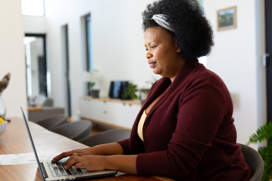 Happy plus size african american woman sitting at table, using laptop