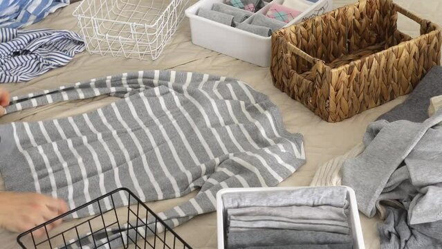 The concept of organizing and storing clothes. A woman folds a sweater and a T-shirt and puts it in a basket.
