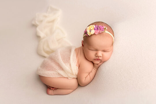Top view of a newborn baby sleeping naked on a white felt background. Beautiful portrait of a little newborn 7 days, one week old. A small newborn angel with a flower headband and white wings.