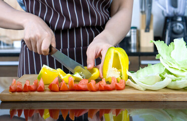Closeup bell pepper and tomato sliced on a wooden chop board. Crisphead Lettuce lay next to it.