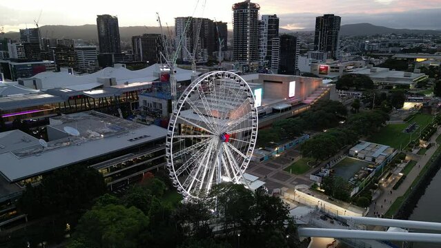 Drone shot of South Bank, shot over Brisbane River, static stationary shot of The Wheel of Brisbane. New Neville Bonner Bridge in construction in background, Sunset.