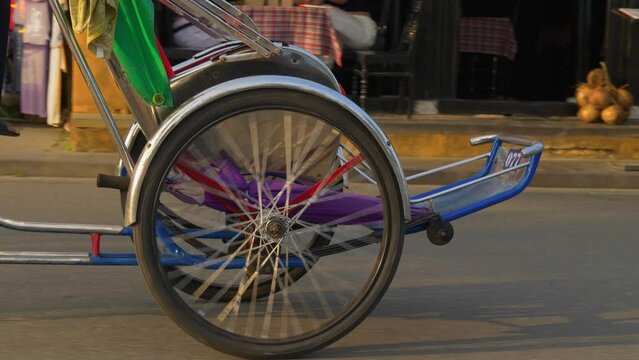 A tracking closeup shot of the wheel of a cyclo rental in Hoi An, Vietnam. You could see the driver pedaling without a passenger.