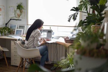 Smiling woman skilled tailor clothes manufacture process on sewing machine posing at workplace