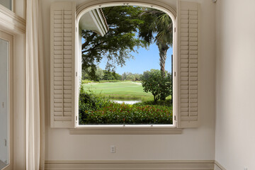 View of Golf Course Through Large Window in Luxury Home Featuring Blue Sky and Luscious Greenery...