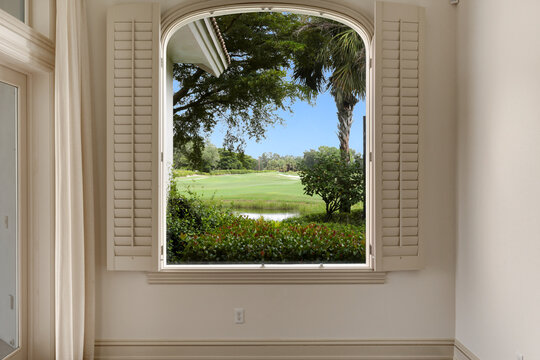 View of Golf Course Through Large Window in Luxury Home Featuring Blue Sky and Luscious Greenery and Palm Trees