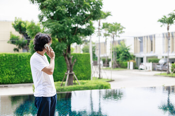 A man remote work during vacation and use smartphone near the swimming pool in resort hotel