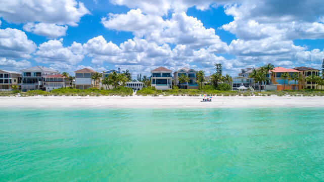 Calm Water Level View of Homes on a Beach in Naples, Florida with Foliage on the Coast and a Blue Sky Featuring Puffy White Clouds