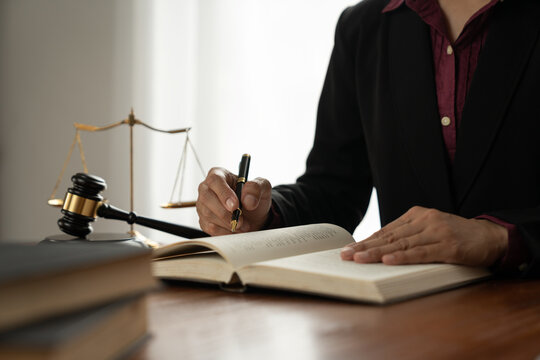 female lawyer, law adviser, businesswoman sitting and reading with finger pointing at legal code information. Business agreement on book working with scales and hammer in office.