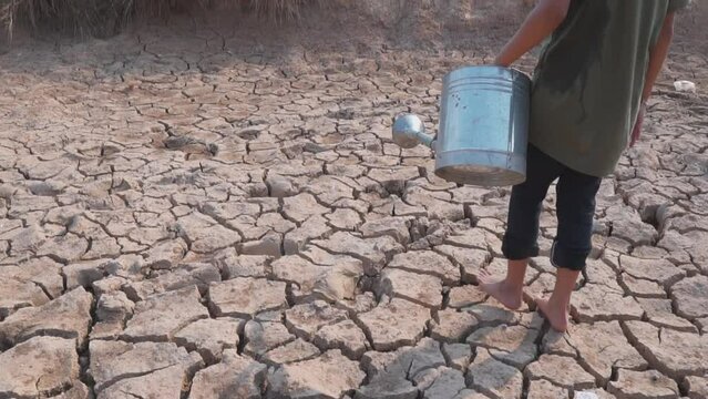  A girl's walking on dry ground. Water crisis, Concept drought and crisis environment.