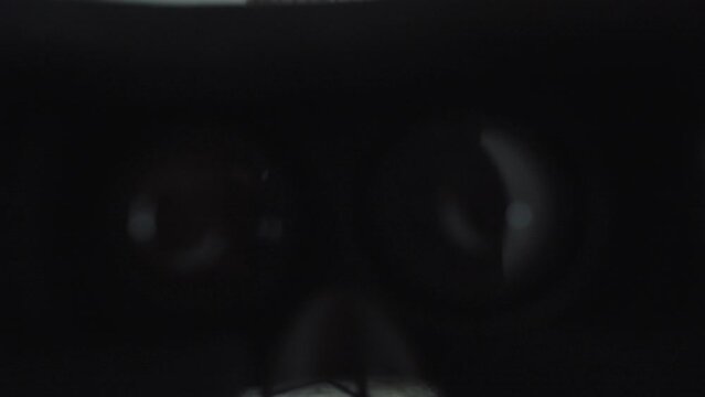 First-person perspective view (point of view POV) holding virtual reality goggles with hands, looks this device over and finally puts it on his head or face.