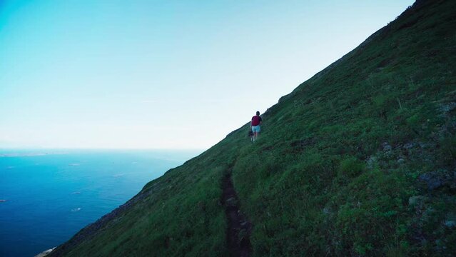 Girl With A Dog Trekking Across Steep Mountains Of Lovund Island, Nordland Norway. Wide Shot