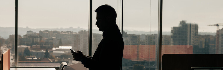 Silhouette of a businessman with phone in his hands standing in office