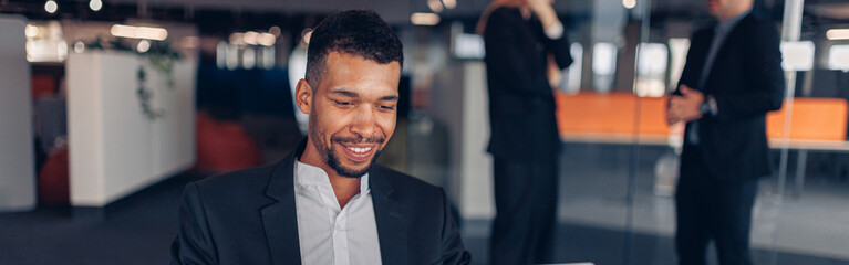 Smiling african businessman working laptop in modern office on colleagues background