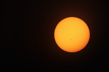 Orange sun on a black background. Big yellow-orange sun with sunspots photographed through a telescope filter on a black background with copy space. selective focus