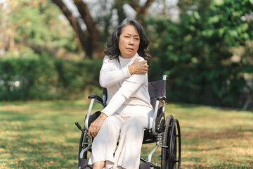 Fototapeta na wymiar Asian old woman sitting on a wheelchair outdoors in the park have shoulder pain