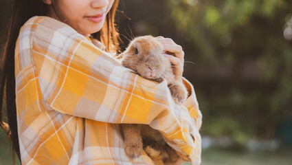Young smiling and innocent girl holding and hugging a cute little rabbit with closed eyes and caressing her on back