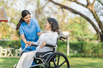 Young asian care helper with asia elderly woman on wheelchair relax together park outdoors to help and encourage and rest your mind with green nature.