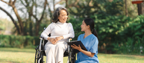 Young asian care helper with asia elderly woman on wheelchair relax together park outdoors to help and encourage and rest your mind with green nature.