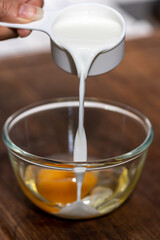 Pouring milk into a bowl that has an egg in it to cook a bakery.