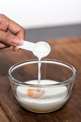 Pouring milk into a bowl that has an egg in it to cook a bakery.