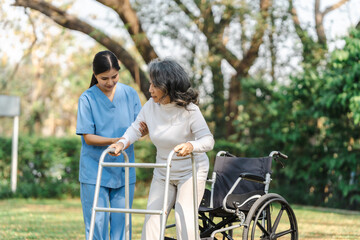 Fototapeta premium Young asian care helper with asia elderly woman on wheelchair relax together park outdoors to help and encourage and rest your mind with green nature. Help support yourself to learn to walk. walker