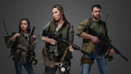 Studio shot of female killer with man and young girl in setting of post apocalypse.