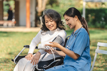 Fototapeta na wymiar Young asian care helper with asia elderly woman on wheelchair relax together park outdoors to help and encourage and rest your mind with green nature. measure blood pressure