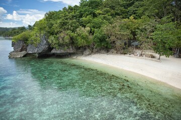 Idyllic, secluded beach of Siquijor in the Philippines with white sand and crystal clear water in a small bay with trees and cliffs.