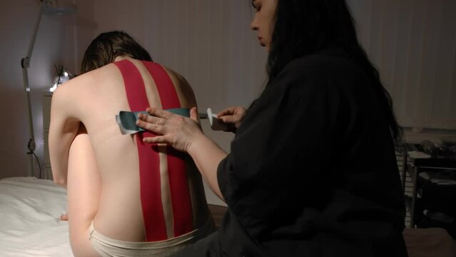 The masseur sticks teips on the back of a young woman