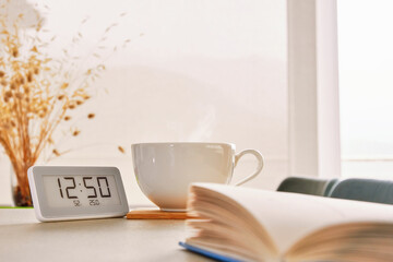 Opened book on the kitchen table with a white cup of hot tea. Cozy interior theme background