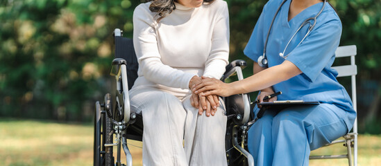 Young asian care helper with asia elderly woman on wheelchair relax together park outdoors to help and encourage and rest your mind with green nature. hold hands to encourage