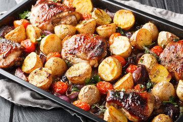 Italian barbecue balsamic chicken with potatoes, red onion and tomatoes close-up on a baking sheet on a wooden table. Horizontal © FomaA