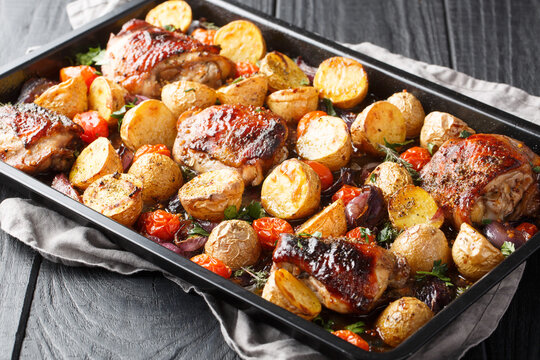Delicious easy sheet pan Balsamic Chicken with Roasted Potatoes, Red Onion, Tomatoes and fresh herbs close-up on a wooden table. Horizontal