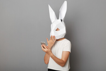 Portrait of shocked astonished anonymous woman wearing white t shirt and paper rabbit mask standing...