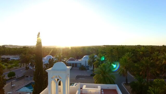 drone shot of a palace in the middle of palm trees at sunset