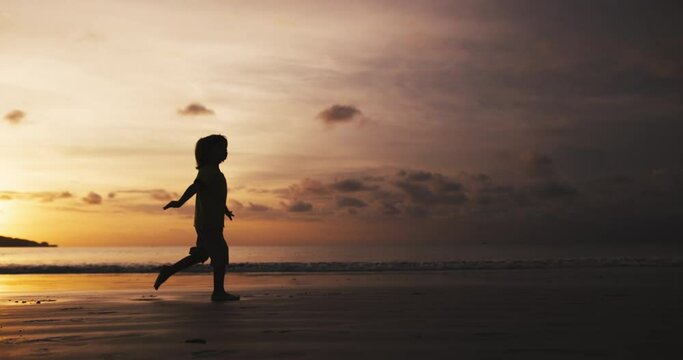 Silhouette of little boy run on the beach spreading hands like airplane, bird