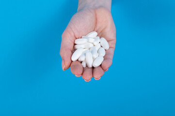 A woman is holding a handful of pills. A woman's hand sticks out of a hole in a cardboard blue background.