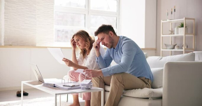 Shocked Young Couple Sitting On Sofa Looking At Bill