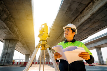 Asian civil engineer working with theodolite and highway construction drawing paper